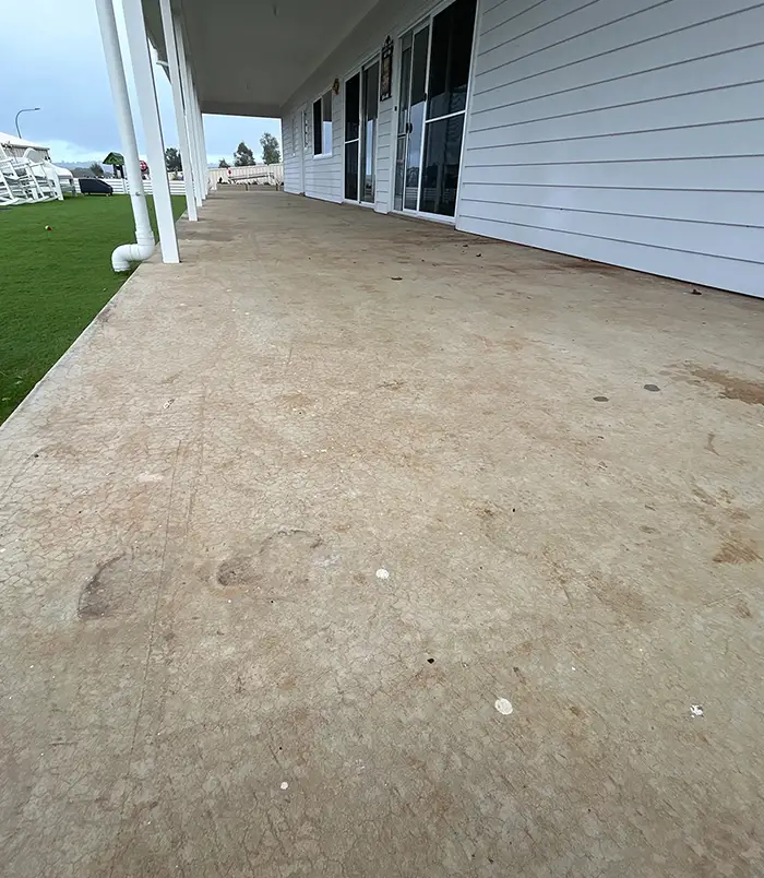 Rough, unsealed concrete veranda floor beside a white weatherboard house and lawn, before epoxy flooring