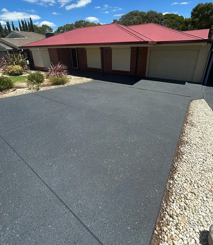 Dark grey resurfaced concrete driveway in front of a brick home with a red roof