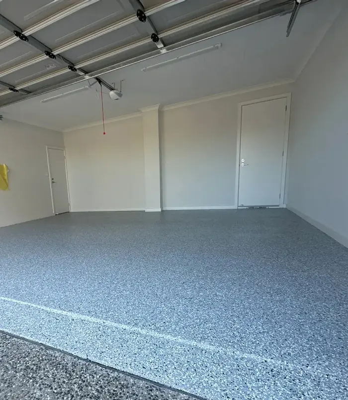 Blue-grey speckled epoxy flake floor in a garage with white walls and a roller door