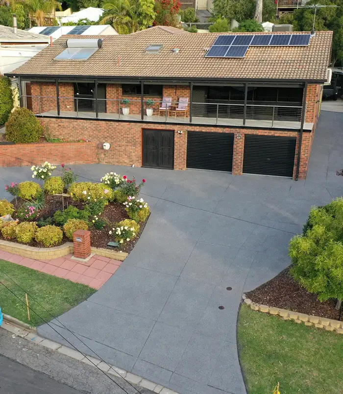 Dark grey resurfaced concrete driveway around a flower garden in front of a two-storey home