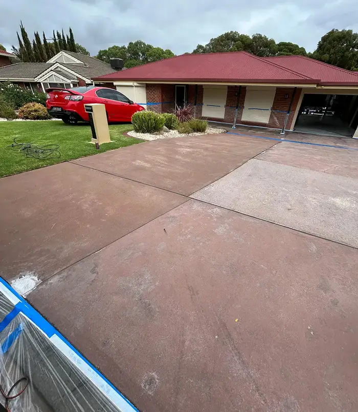 Faded, patchy pink concrete driveway in front of a brick home with a red roof, before resurfacing