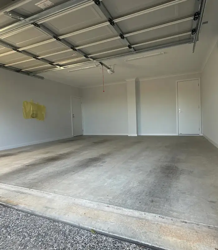 Bare concrete garage floor with white walls and a roller door, before epoxy flooring