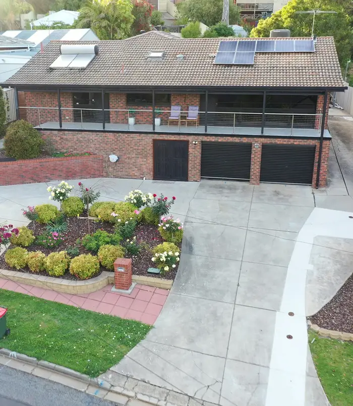 Pale concrete driveway around a garden bed in front of a two-storey home, before resurfacing