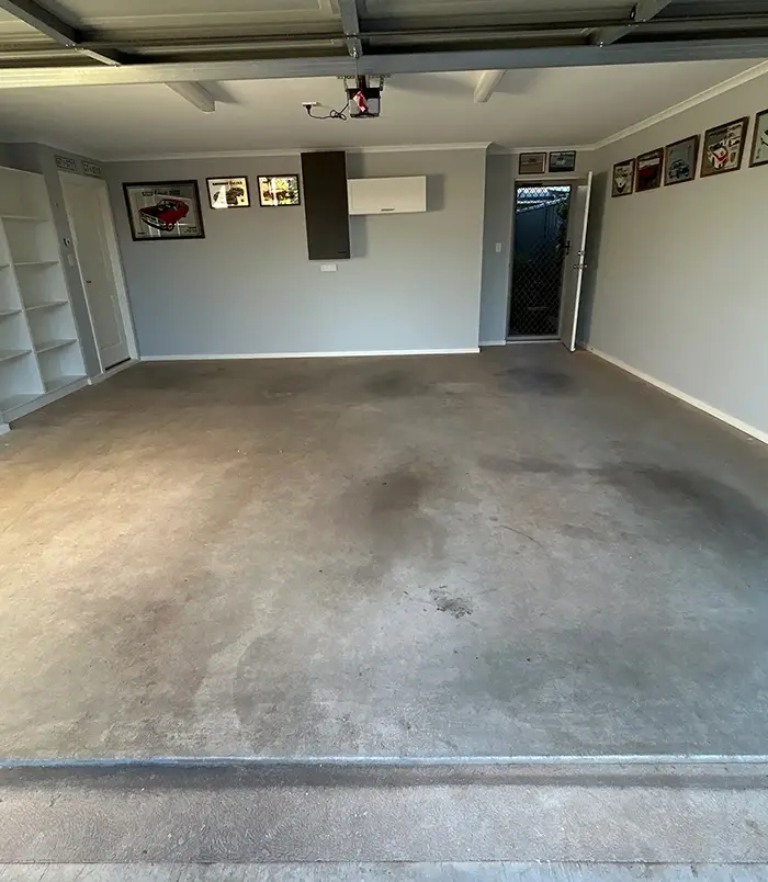 Dirty, oil-stained concrete floor in a garage with built-in shelving, before epoxy flooring