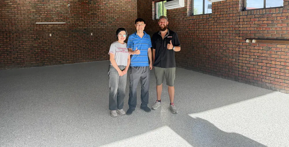 Surface Rescue technician posing with two customers on a speckled epoxy floor in a garage