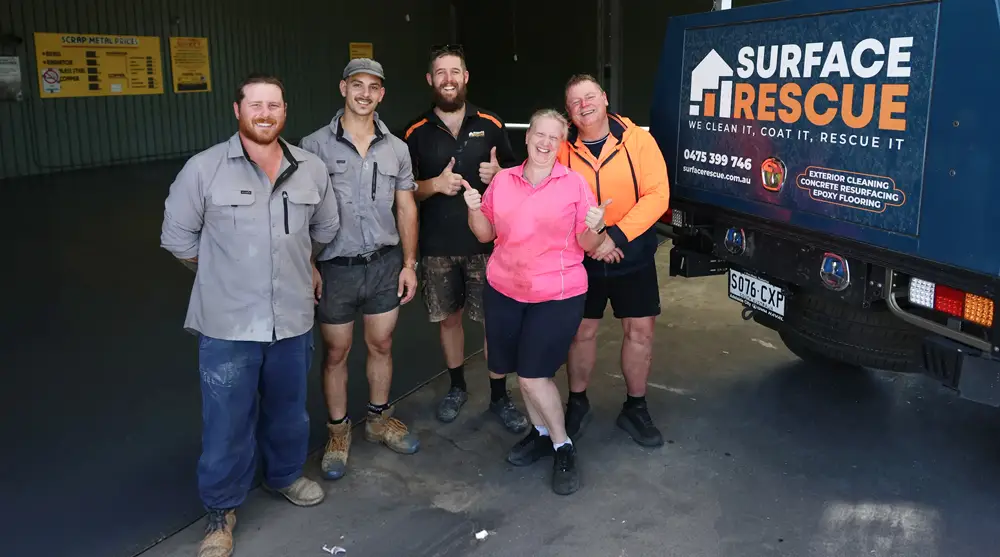 Surface Rescue team members and a customer in a bright pink top posing in front of a branded van