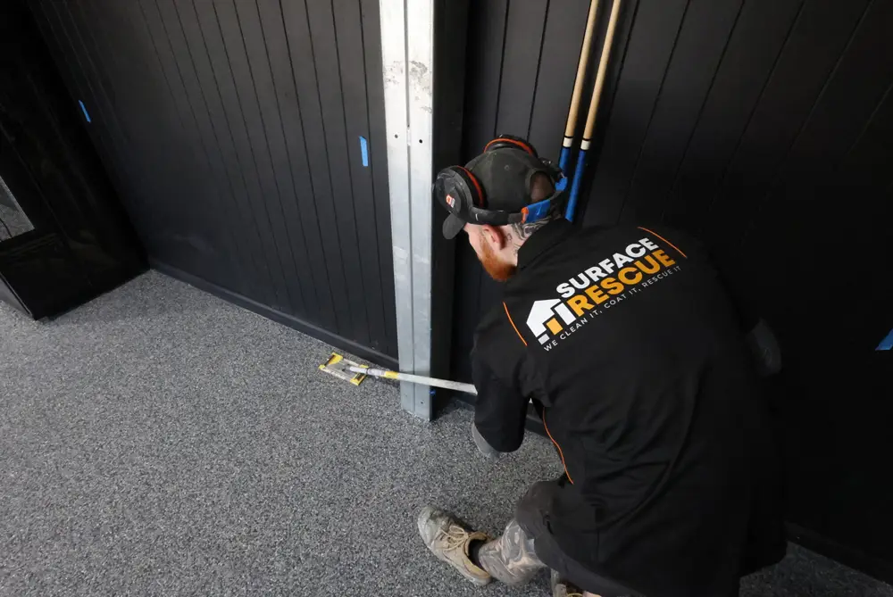Surface Rescue technician in a black uniform and cap working along a wall edge on a speckled floor