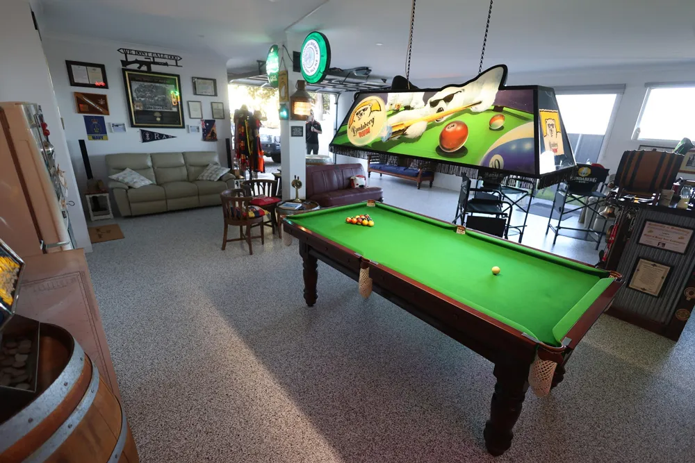 Games room with a green pool table, lounge seating and memorabilia on a speckled epoxy flake floor