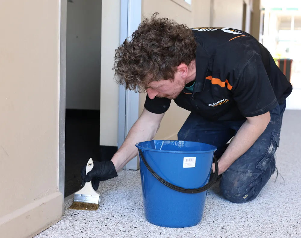 Surface Rescue technician crouching beside a blue bucket to clean a white floor surface