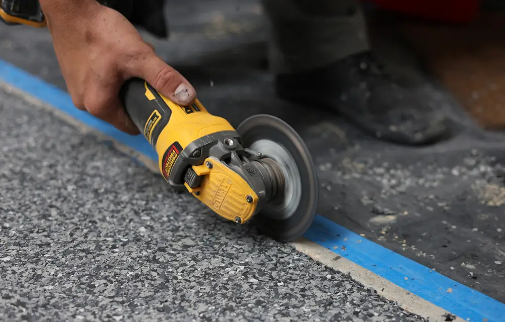 Yellow angle grinder preparing a concrete surface beside blue masking tape