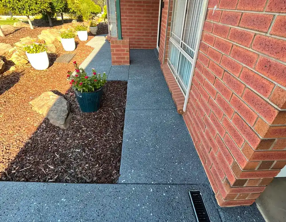 Blue-grey resurfaced concrete path beside a red brick wall and potted plant