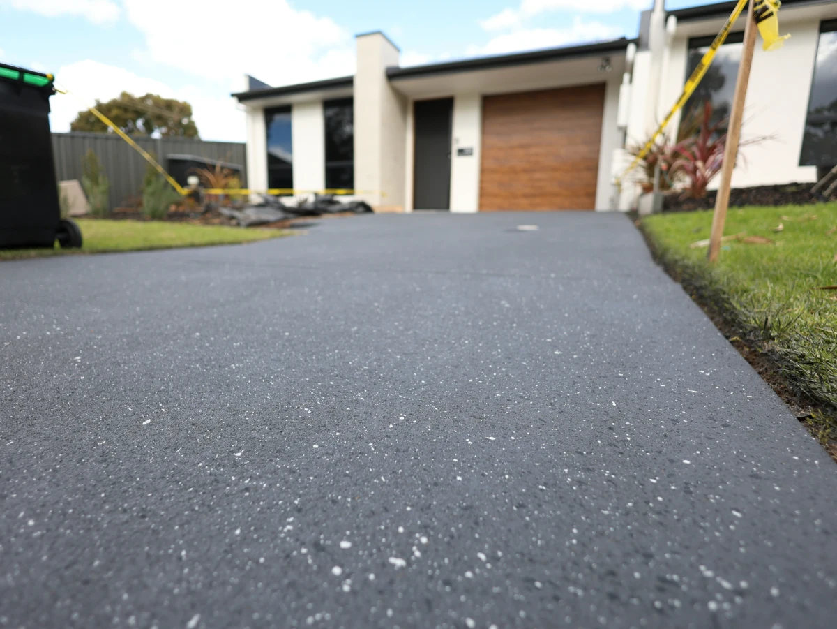Dark grey resurfaced concrete driveway in front of a modern home with a timber garage door