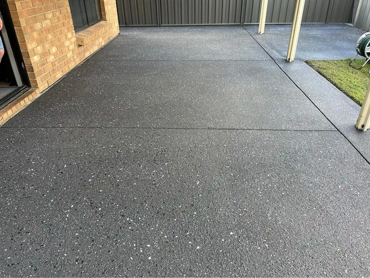 Dark speckled resurfaced concrete beside a metal fence and carport