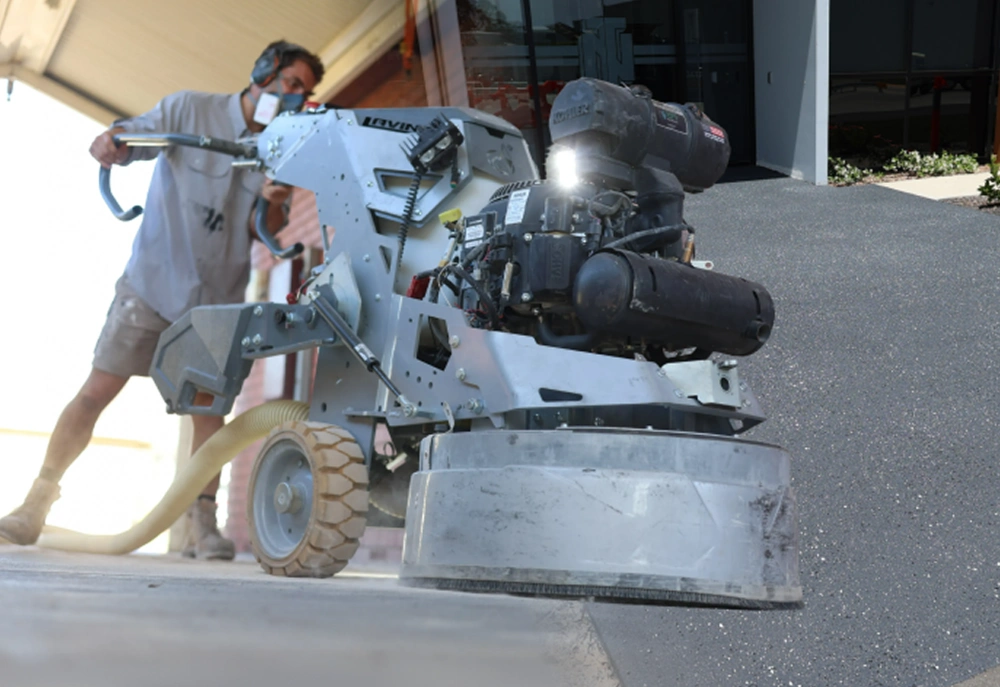 Surface Rescue technician wearing a dust mask operating a concrete grinder to prepare a floor