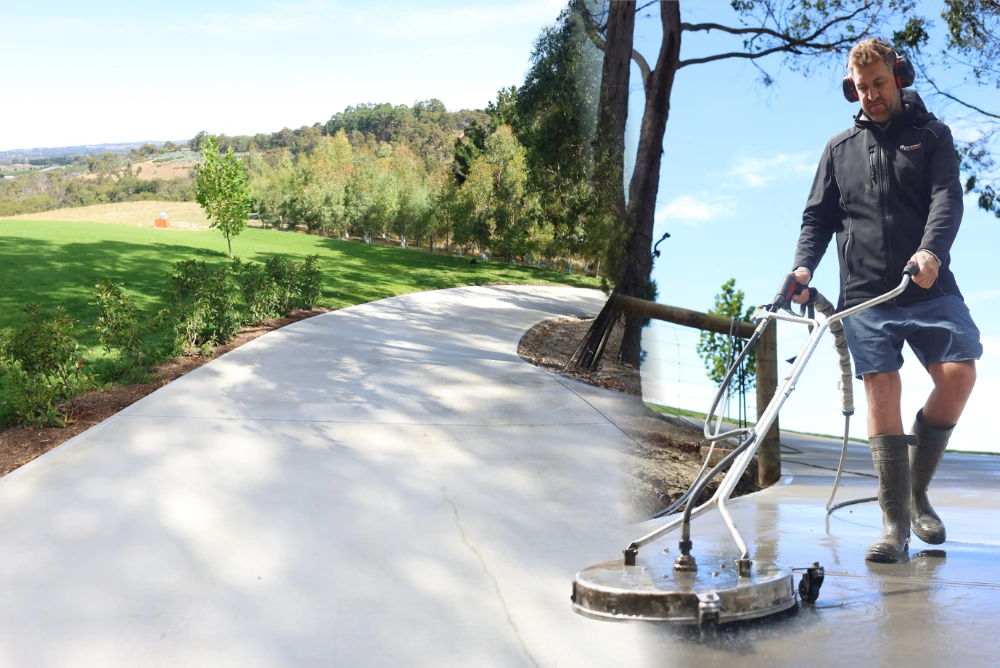 Surface cleaner machine cleaning a pale concrete path curving past lawn and trees