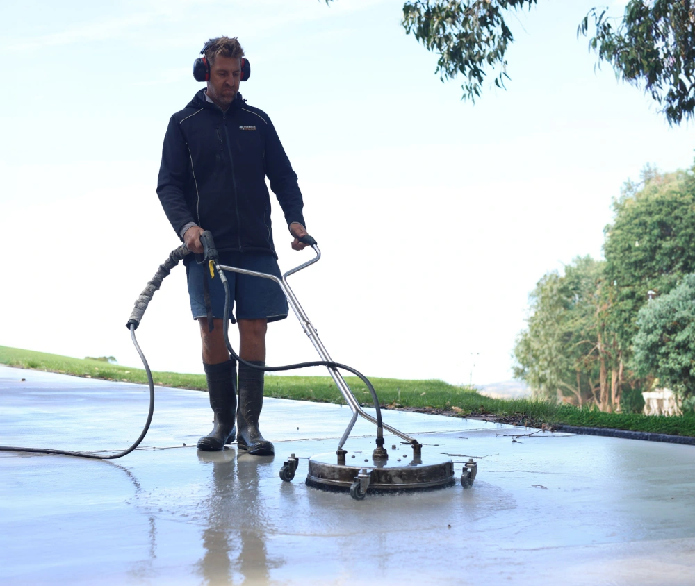 Surface Rescue technician using a surface cleaner on wet concrete under a blue sky