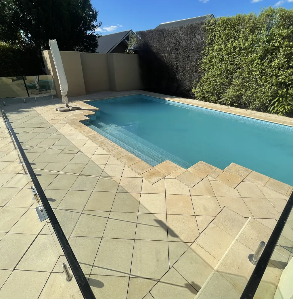 Golden pavers and steps around a swimming pool beside a hedge wall