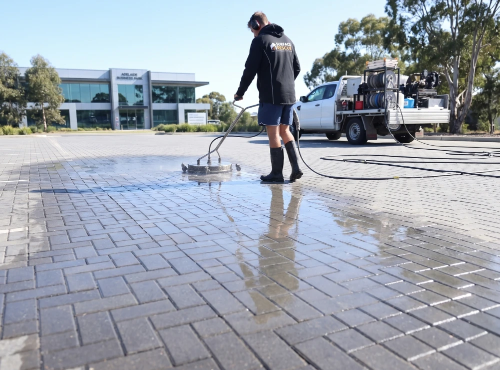 Surface Rescue technician using a surface cleaner on wet pavers outside a commercial building