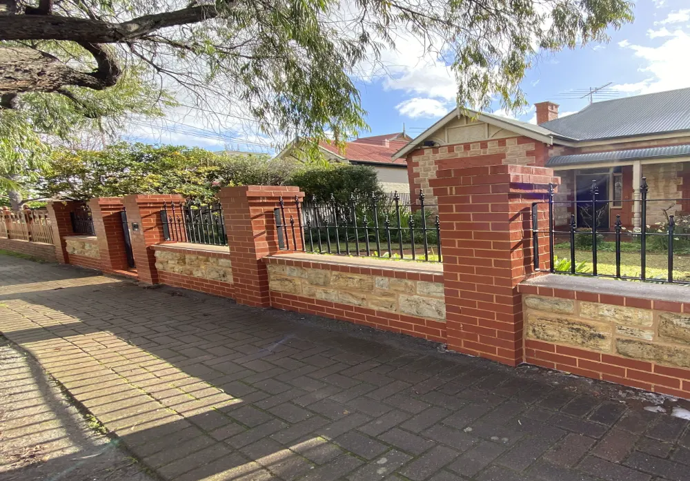Red brick and sandstone front fence with black iron panels in front of a heritage home