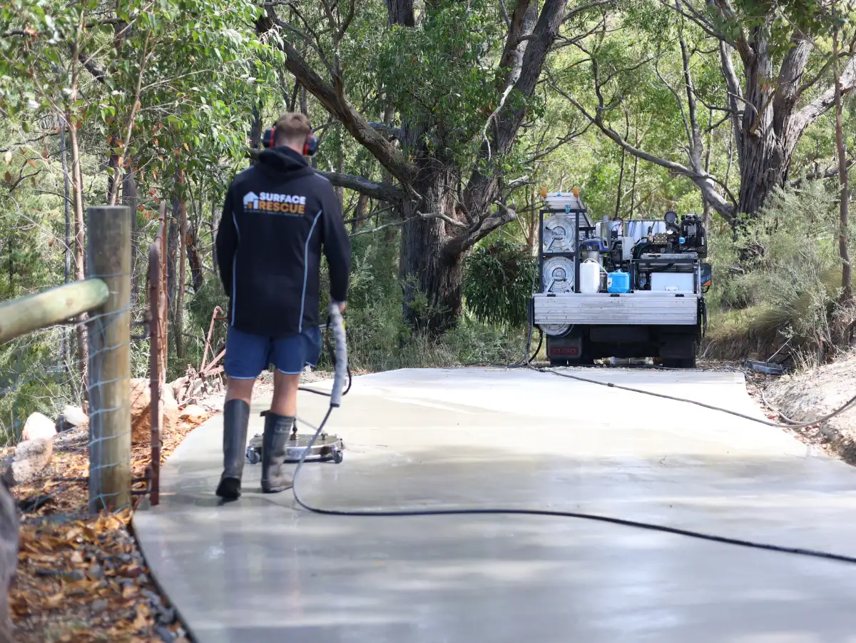 Surface Rescue team member operating a surface cleaner on concrete, with a pressure washing unit in the background