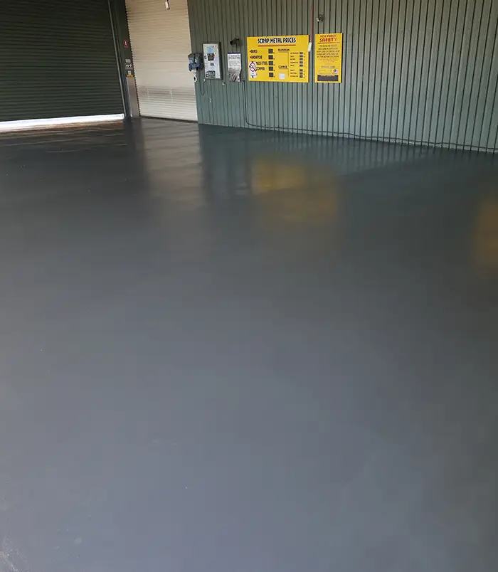 Glossy dark grey epoxy floor in an industrial building with yellow signs on the wall