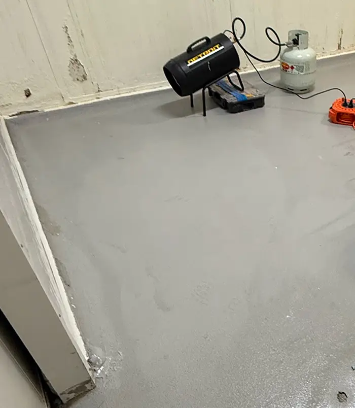 Bare concrete floor in an industrial space with a heater and gas bottle, before epoxy flooring