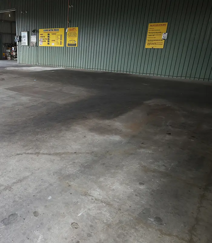 Stained, dusty concrete floor in an industrial building with yellow signs, before epoxy flooring
