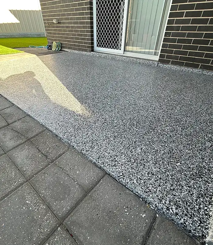 Grey speckled epoxy flake patio floor beside a dark brick wall and sliding door