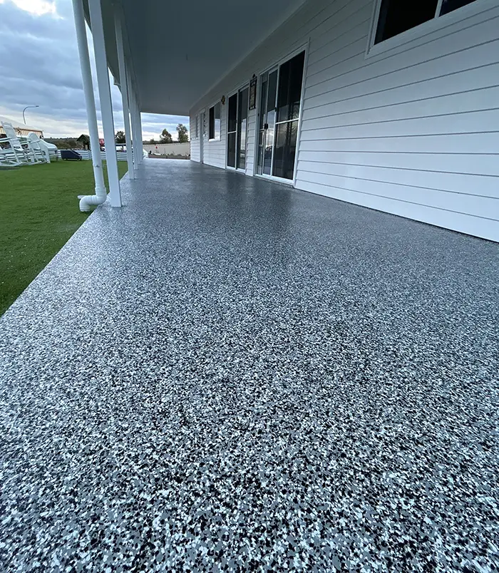 Blue-grey speckled epoxy flake veranda floor beside a white weatherboard house and lawn