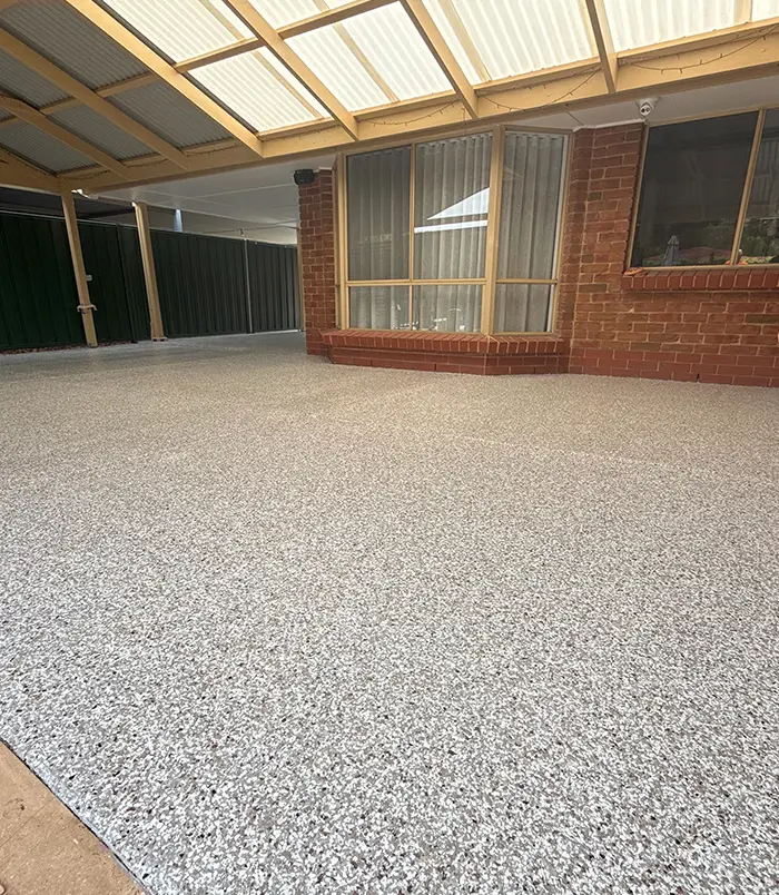Speckled grey epoxy flake patio floor under a pergola beside a brick wall