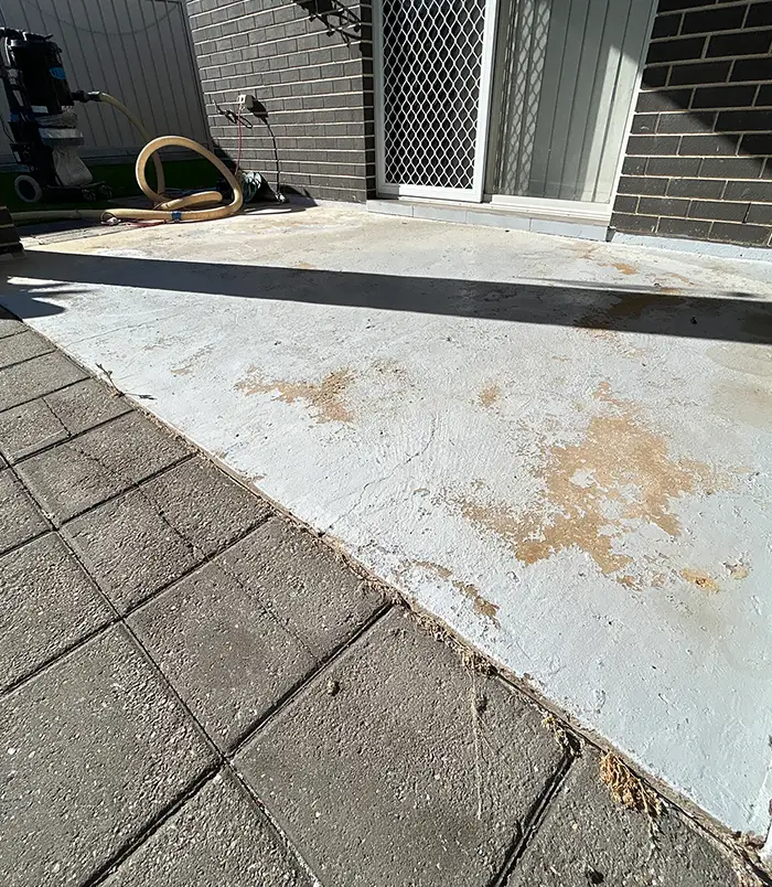 Stained, rust-marked concrete patio beside a dark brick wall and paving, before epoxy flooring