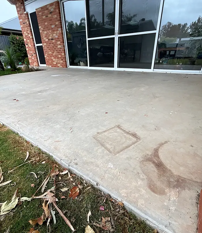 Pale, stained concrete patio beside a brick home with large glass doors, before epoxy flooring