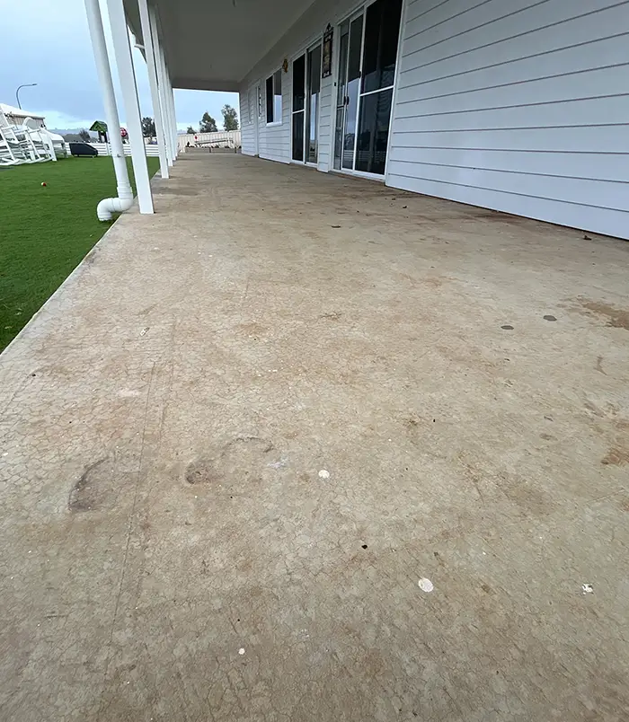 Rough, unsealed concrete veranda floor beside a white weatherboard house and lawn, before epoxy flooring
