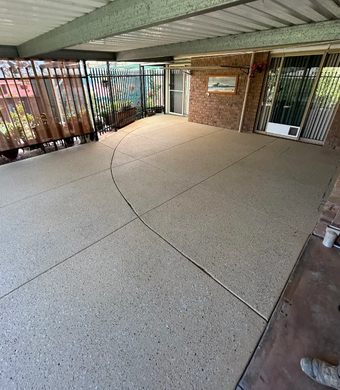 Clean, even resurfaced concrete patio under a pergola beside a black fence and glass door