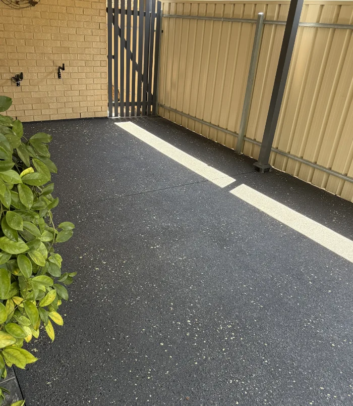 Dark speckled resurfaced concrete courtyard beside a gate, fence and plants