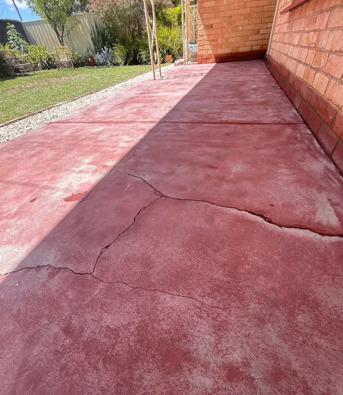 Faded, cracked pink concrete path beside a brick wall and lawn, before patio resurfacing