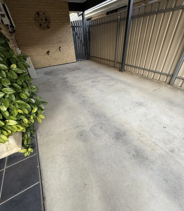 Pale, stained concrete courtyard beside a brick wall and metal fence, before patio resurfacing
