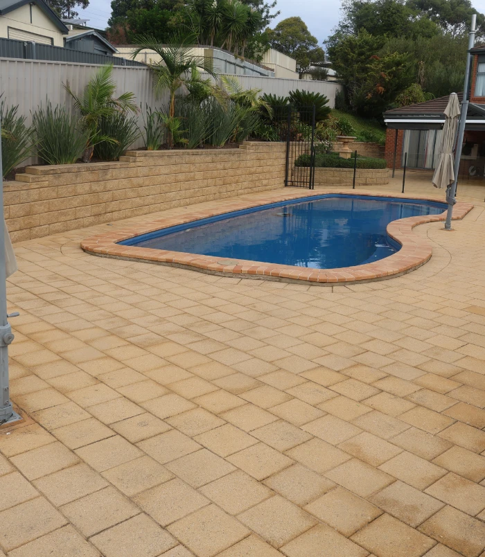 Clean, warm-toned brick pavers around a freeform blue swimming pool