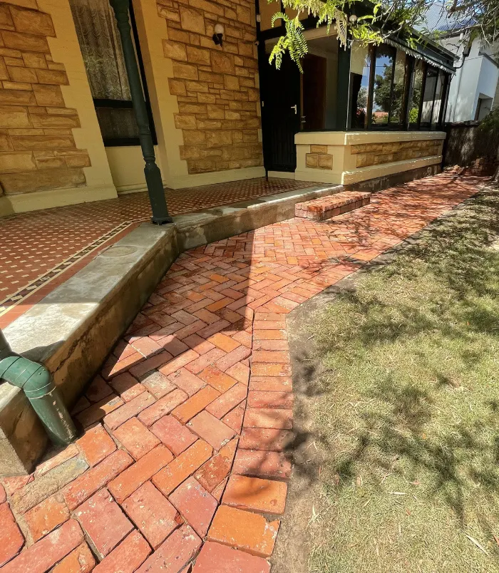 Clean red brick paving beside a sandstone house and lawn