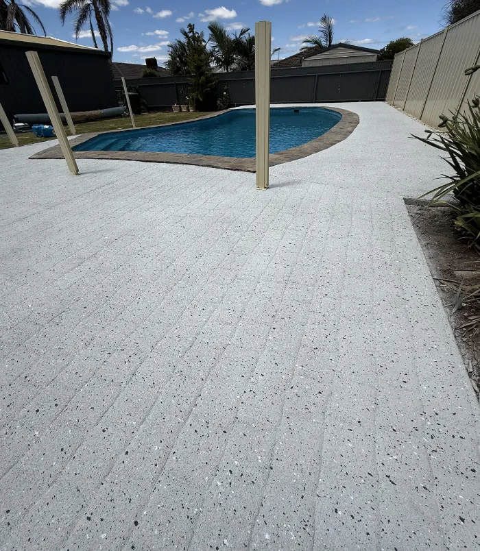 Clean, light resurfaced pool surround around a freeform swimming pool with a safety fence