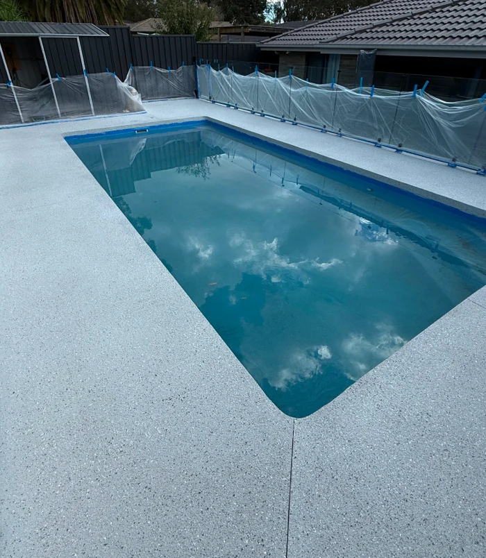 Light, speckled resurfaced pool surround beside a swimming pool with a safety fence