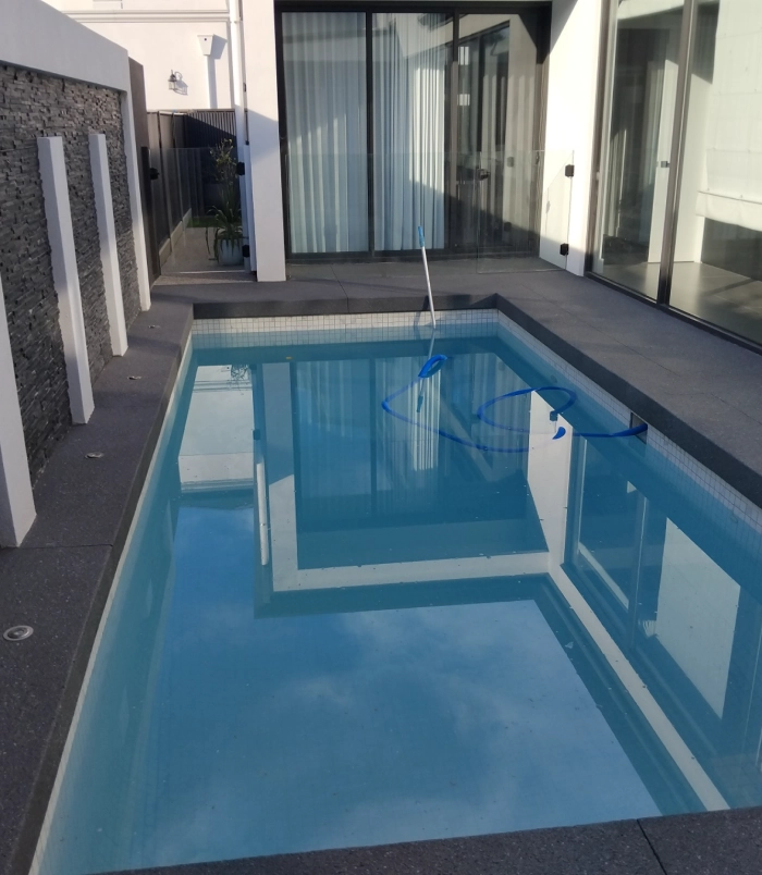 Dark resurfaced pool surround beside a rectangular swimming pool and glass doors
