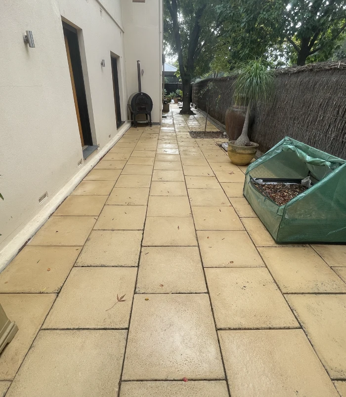 Clean, golden pavers in a side courtyard beside a rendered wall and garden bed after pressure washing