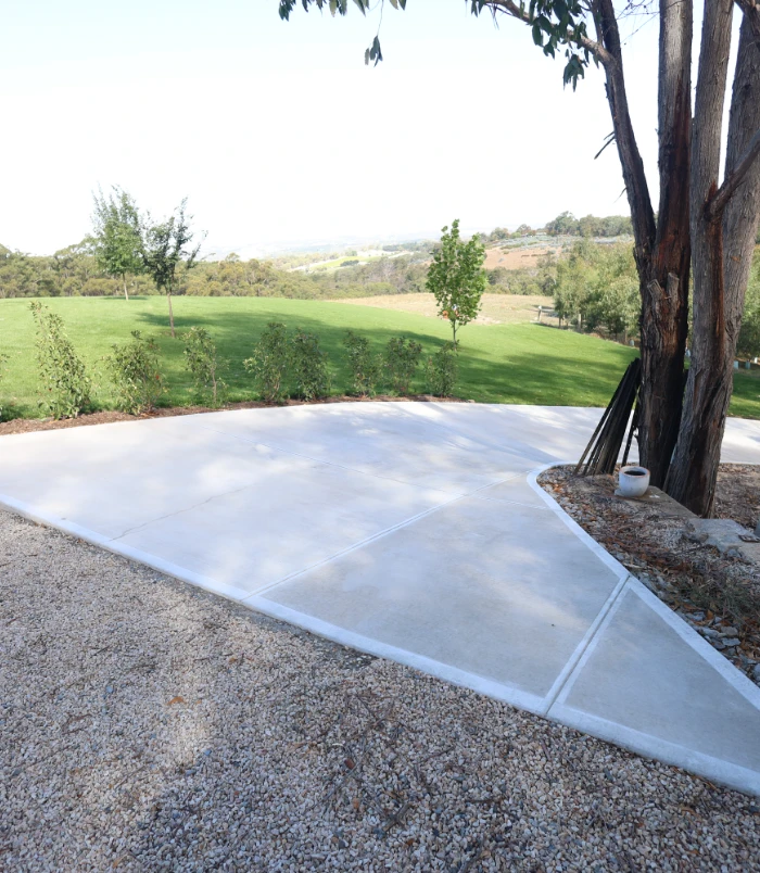 Freshly sealed concrete slab with a clean, bright finish next to a gum tree and grassy hill