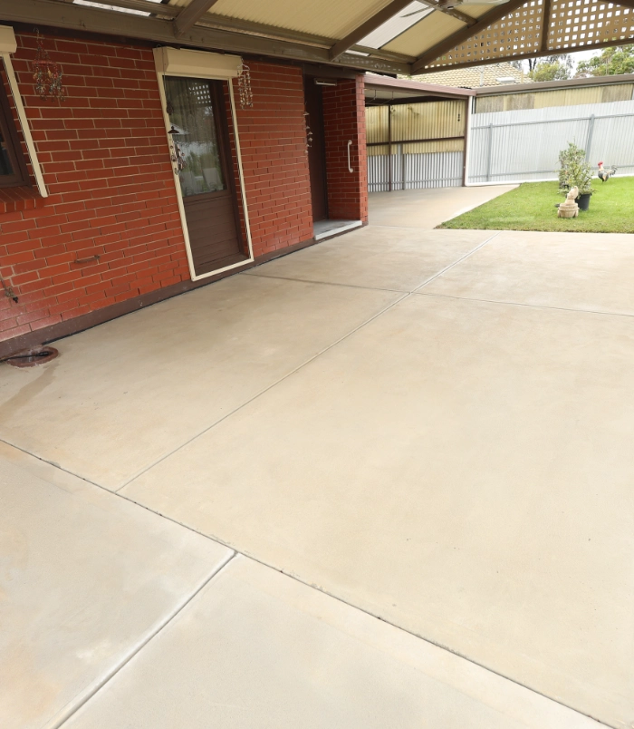 Concrete patio beside a red brick home after sealing, with a clean, uniform cream finish