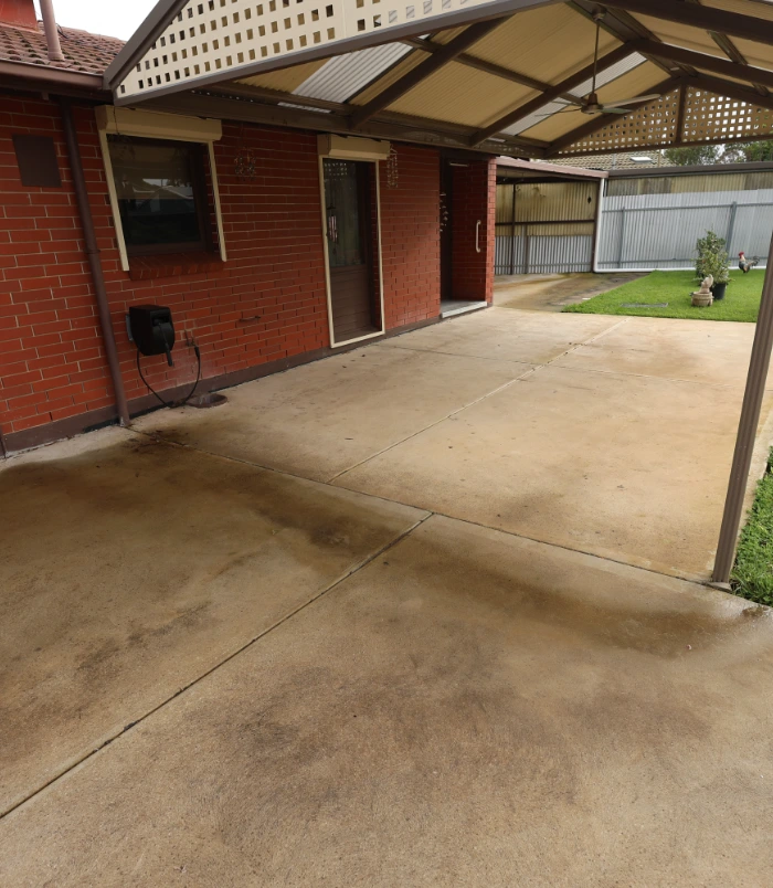 Concrete patio beside a red brick home before sealing, with dirty, patchy staining