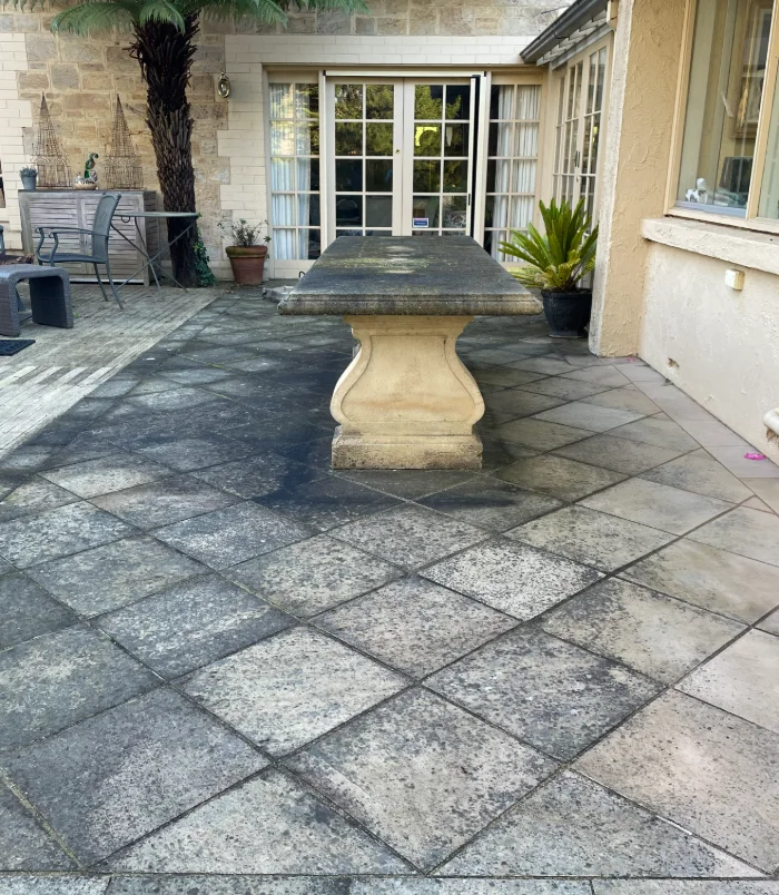 Dull, stained grey pavers before sealing, around a stone outdoor table